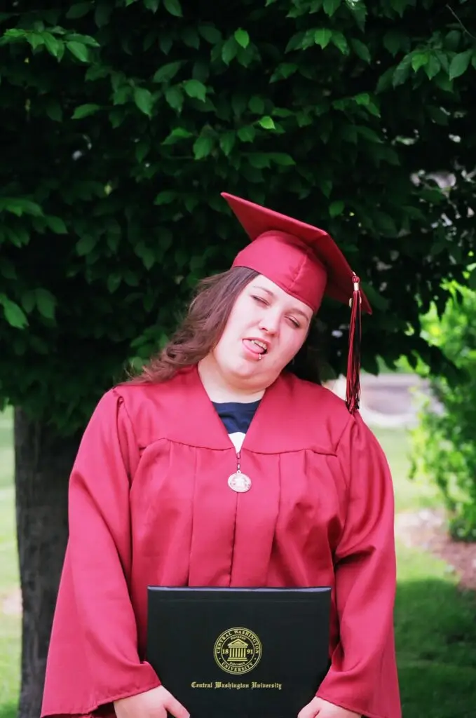 Me in my cap and gown at my college graduation, making a face with my eyes closed and sticking my tongue out.