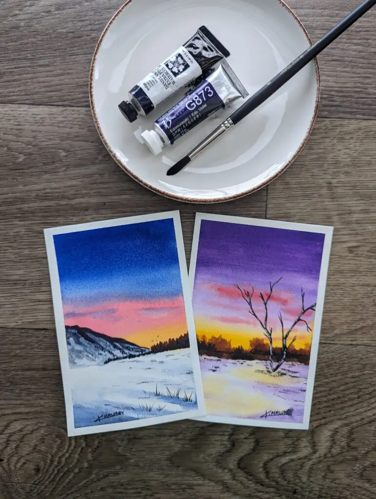 two watercolors paintings. one is of a snowy mountain with a pink orange and blue sunset. The other painting is a purple sunset with a bare tree in the foreground of a snow field.