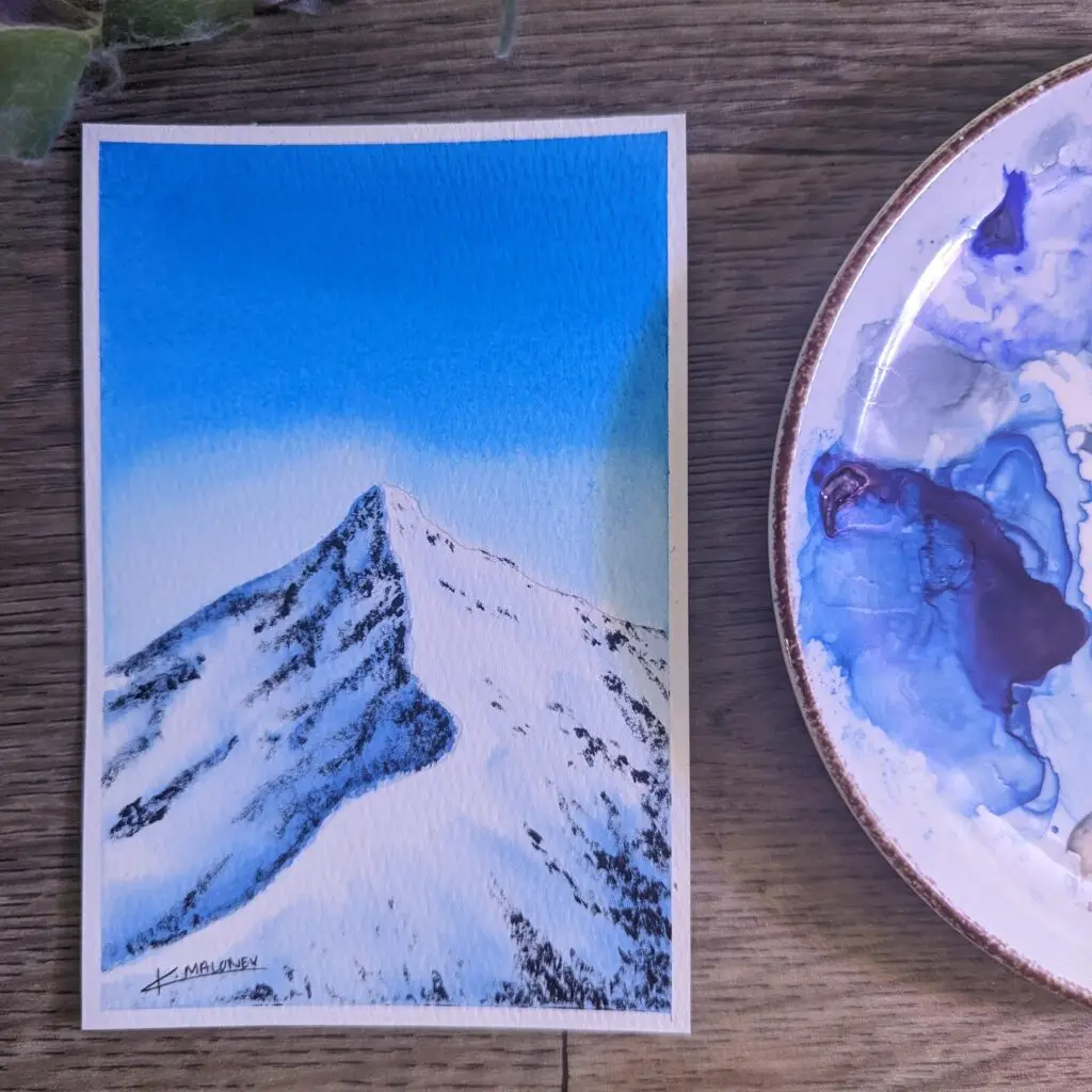 A watercolor painting with a light blue sky, and a mountain peak in the foreground. The mountain is shaded on the left to make it appear to be the ridgeline.