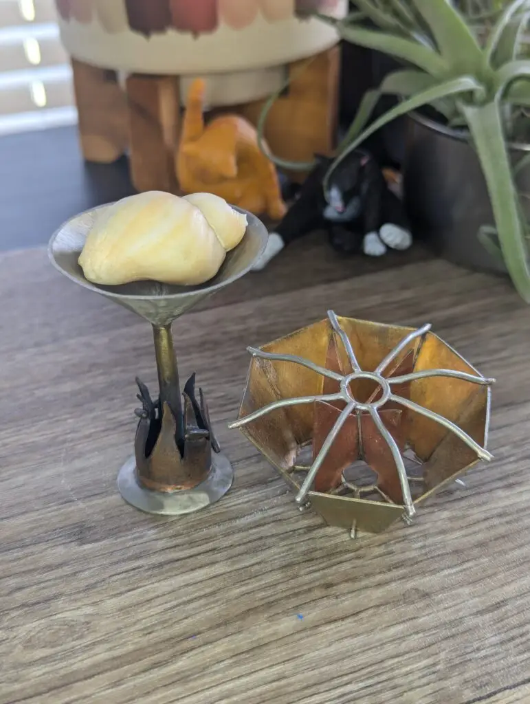 a metal martini glass with flames around the base, with a seashell sitting in the cup. Next to a octagon abstract brooch