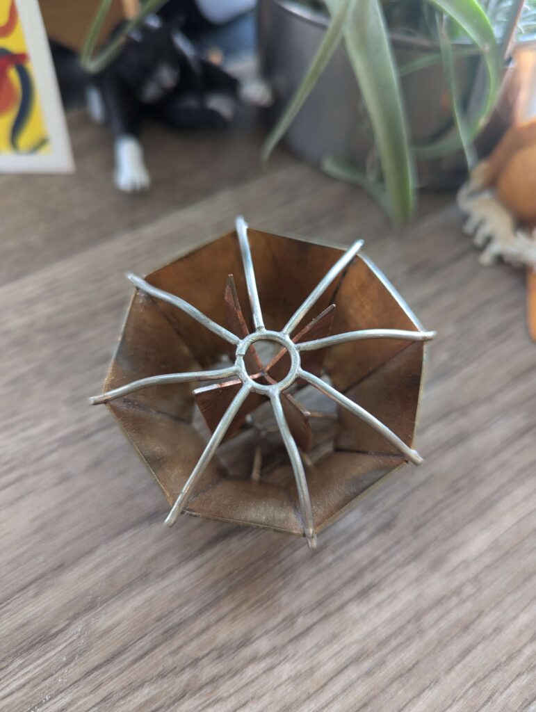 Octagon shaped brass brooch with a copper inner design and a silver cage on top 