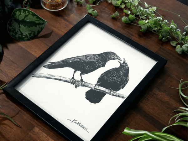 An up close image of the crow family is an 8x10 frame. The Crow Family art print is a black and white image of two crows. The one on the left is looking at the one on the right which has it's mouth open like it has something to say. The art print is surrounded by green plants.