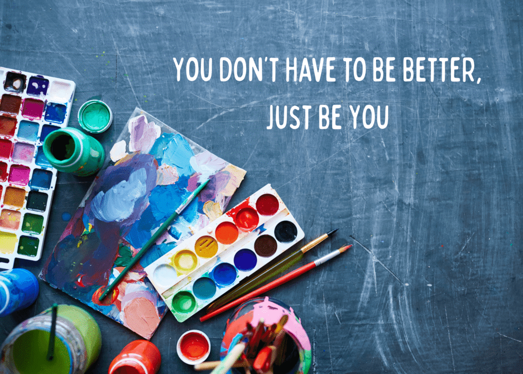 Flat lay of colorful watercolor paints, brushes, and jars of paint on a dark textured background with the words: ‘You don’t have to be better, just be you,’ highlighting the theme of overcoming comparison in art